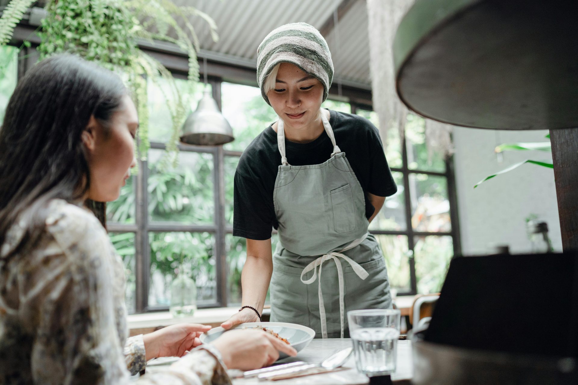 Waitress in uniform serving a meal to a customer in a charming cafe with lush greenery.