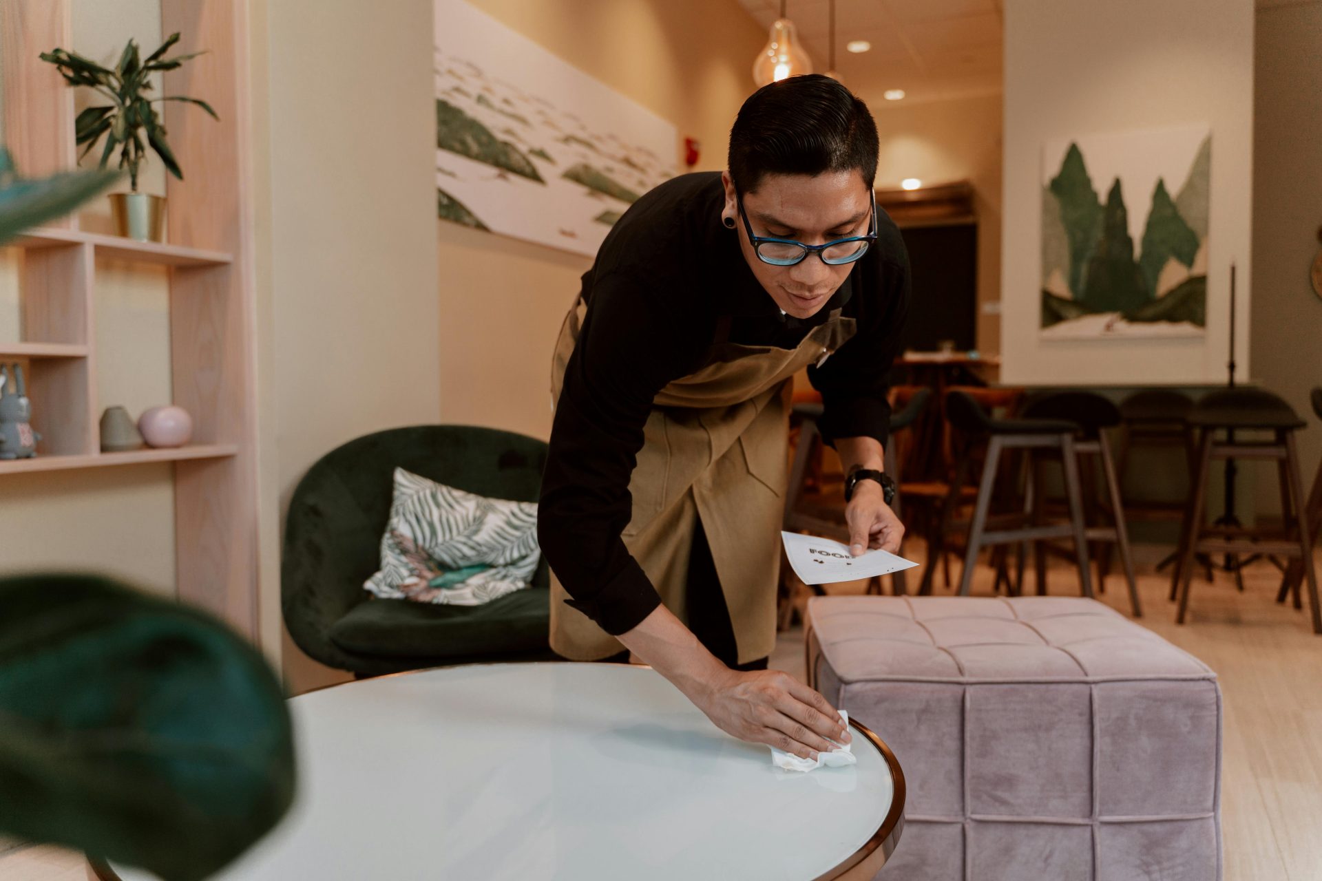 A barista wipes down a table in a stylish café interior, showcasing cleanliness and hospitality.